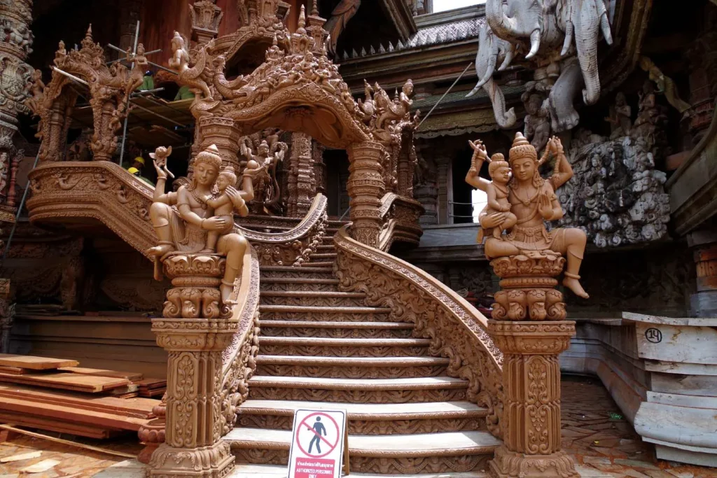 Intricate wooden temple entrance with detailed carvings of seated mythical figures and stairs.

