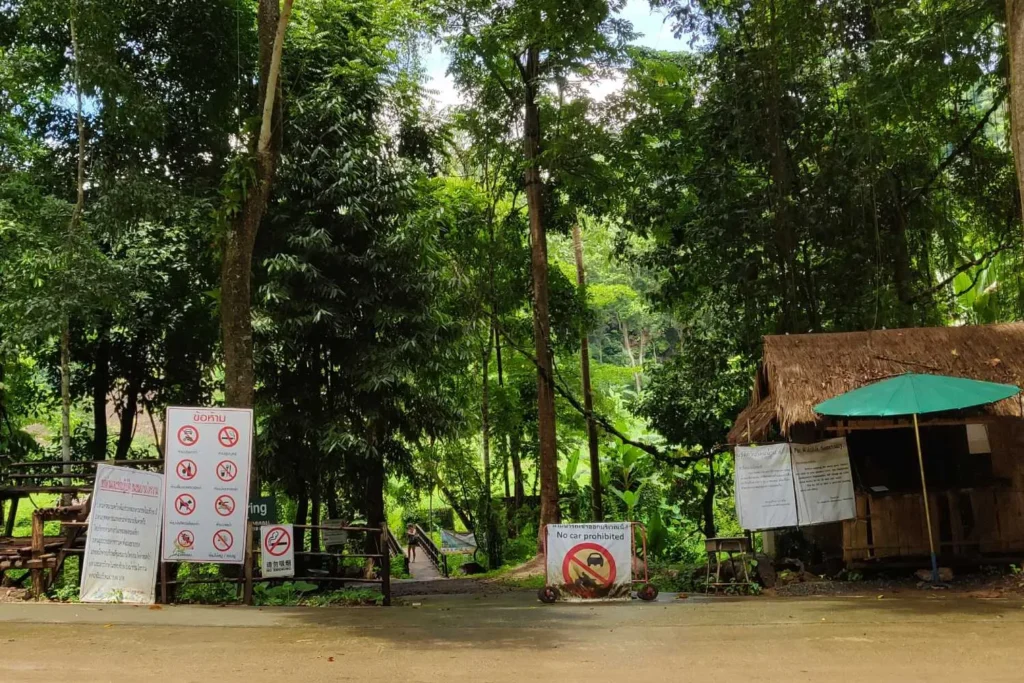 Entrance to a lush green forest park with multiple no-smoking and no-littering signs visible.

