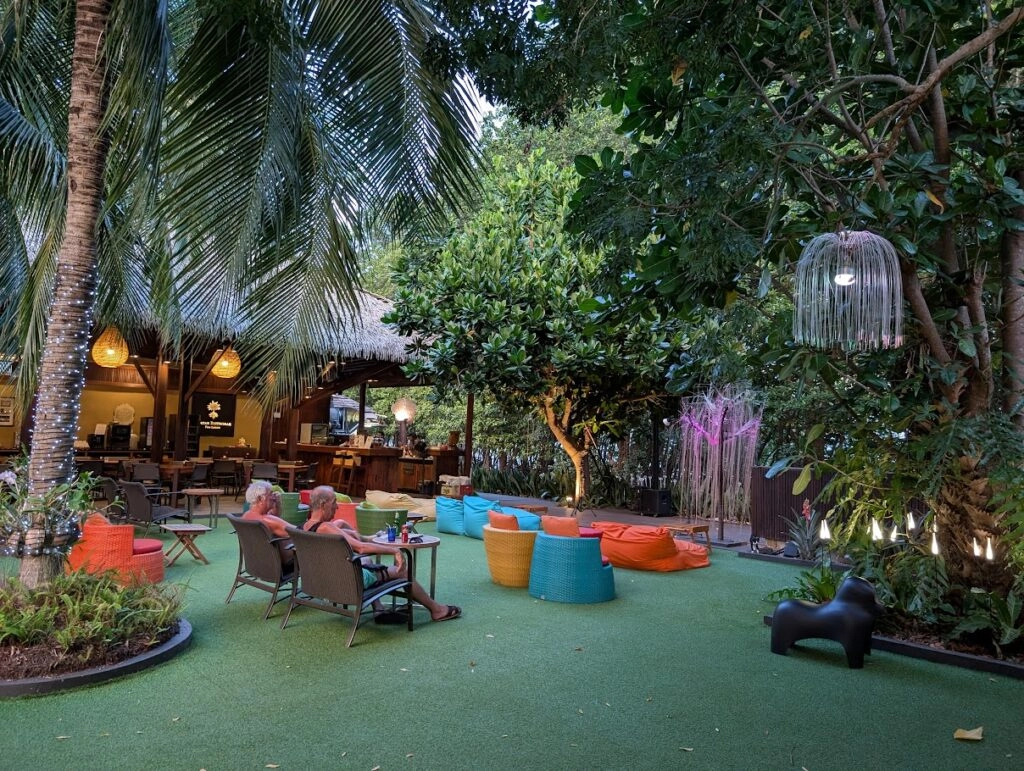 Outdoor tropical garden lounge with colorful seating, palm trees, and warm lighting at dusk