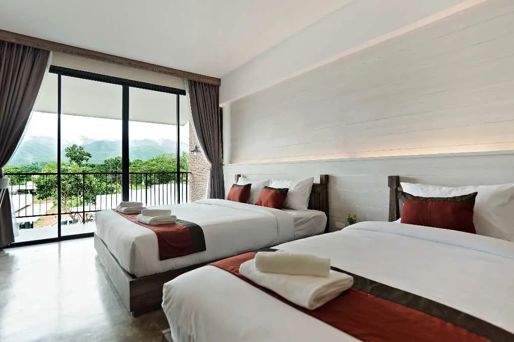 Modern hotel room with two beds, balcony, and scenic mountain view through glass doors