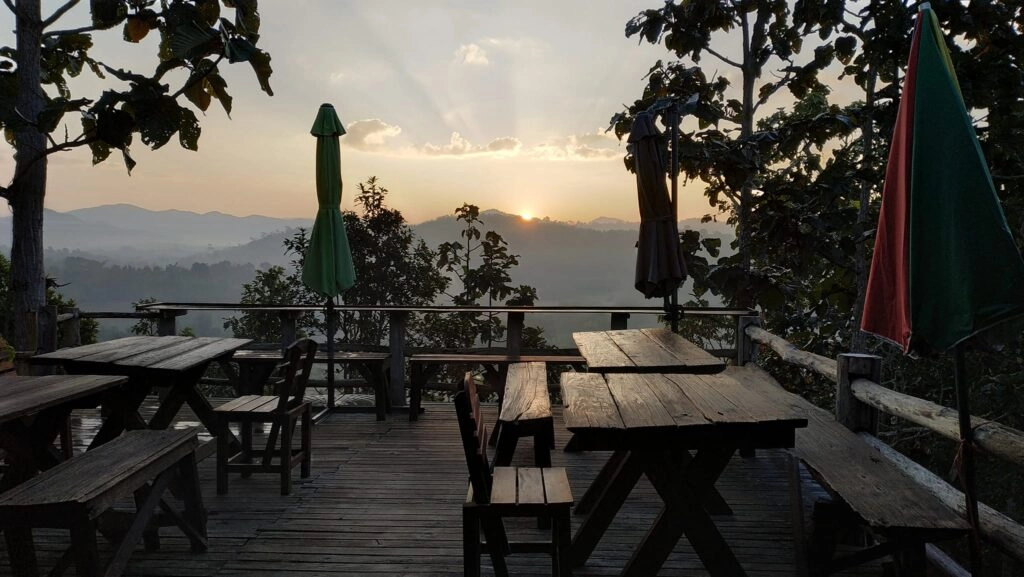 Sunset view over mountains from outdoor wooden terrace with empty tables and umbrellas