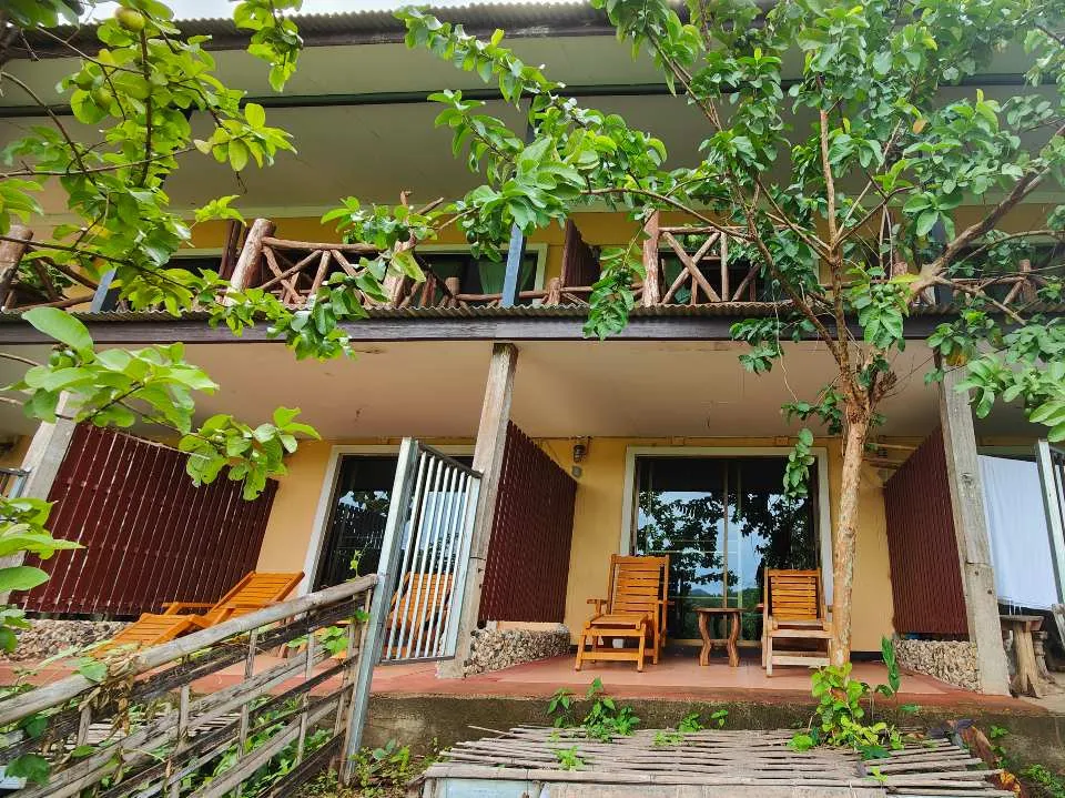 Balcony and patio seating area of a tropical lodge surrounded by lush green trees and plants.

