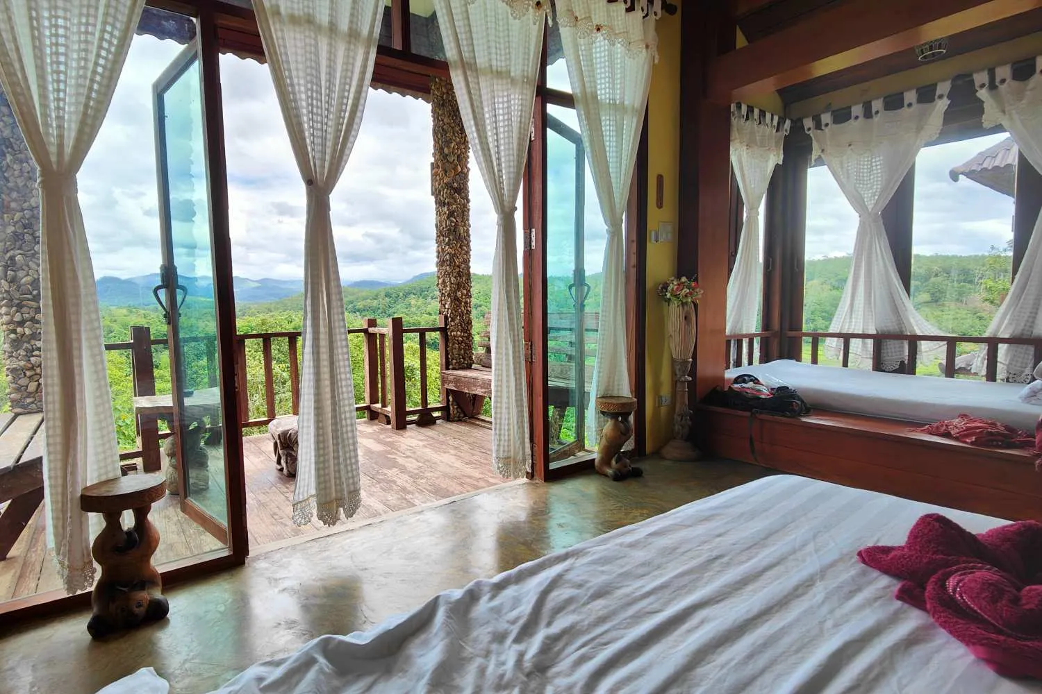 Cozy bedroom with large windows and curtains overlooking a green mountain landscape.