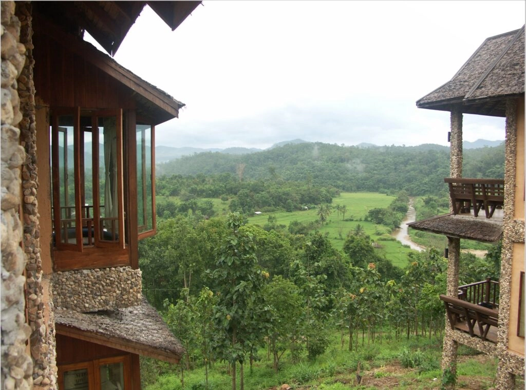View of lush green valley and hills between two rustic wooden lodges under cloudy sky