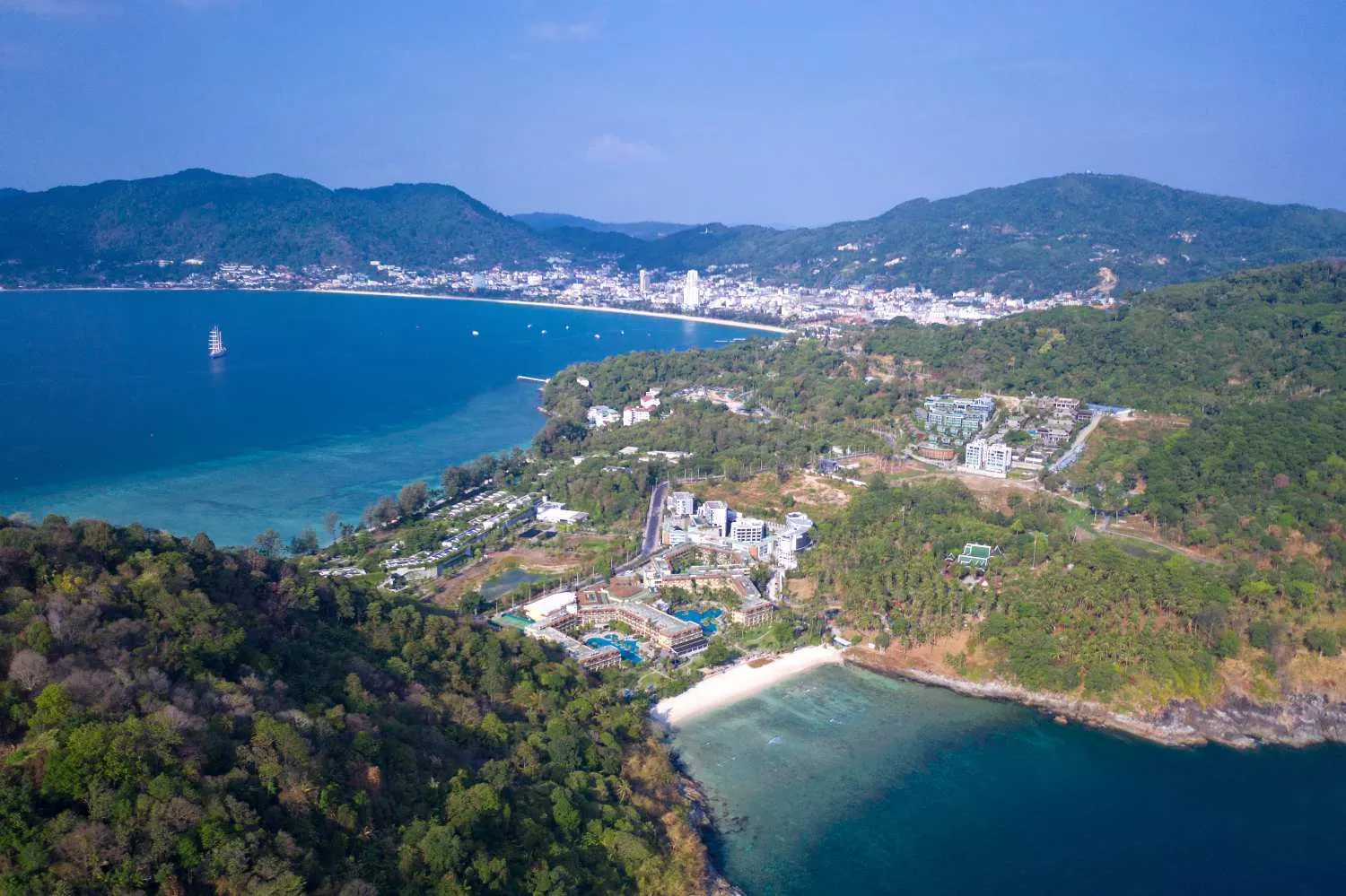 Aerial view of a coastal town with green hills, beaches, and blue ocean under clear sky

