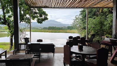Covered outdoor seating area overlooking a river, trees, and distant mountains on a cloudy day

