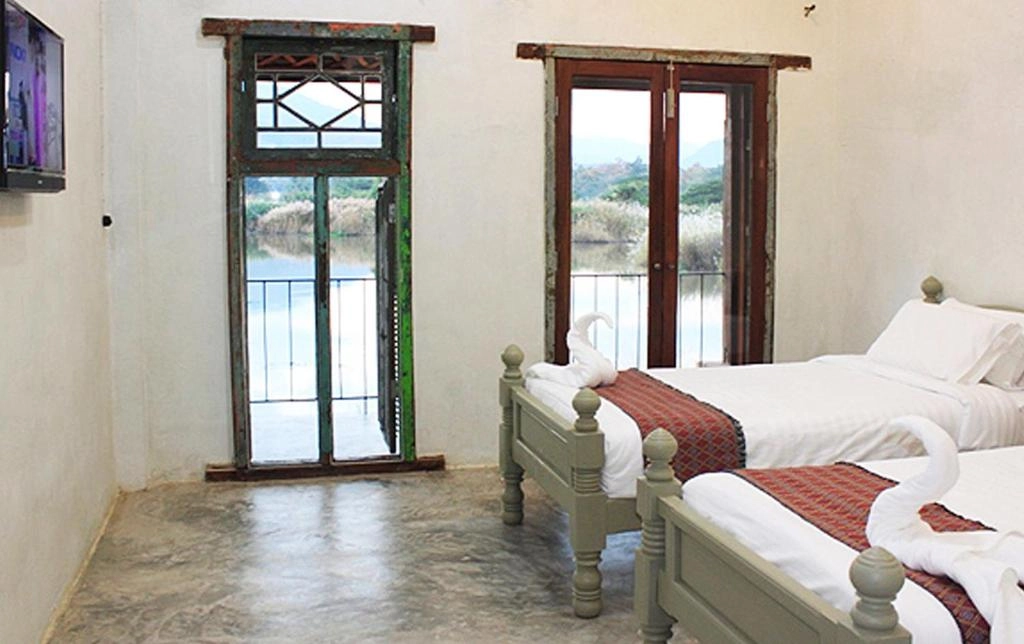 Cozy twin beds in rustic room with open doors overlooking lake and hills outside