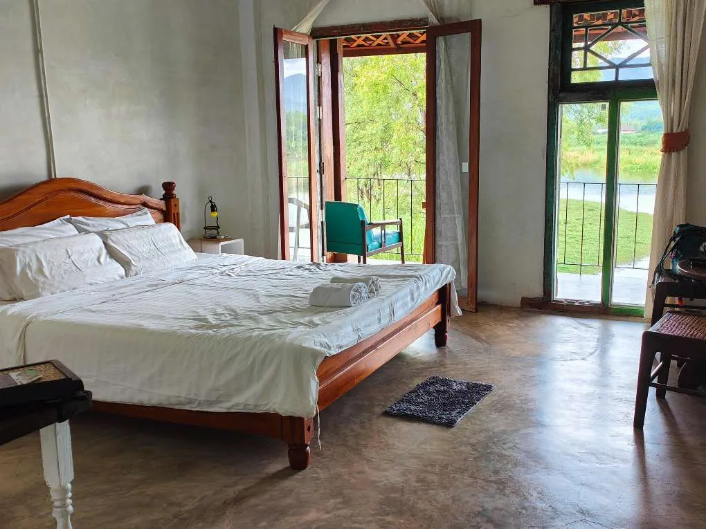 Cozy bedroom with wooden bed, white linens, open doors leading to green outdoor balcony.