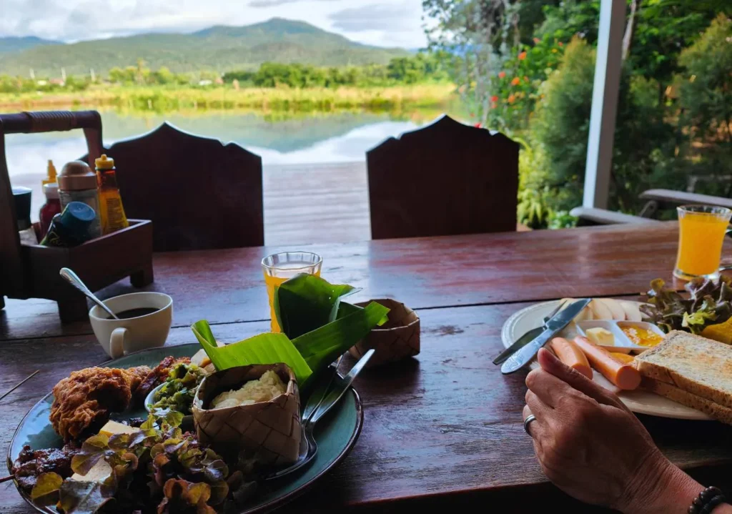 Breakfast with toast, juice, and local dishes on a wooden table overlooking a lake and mountains