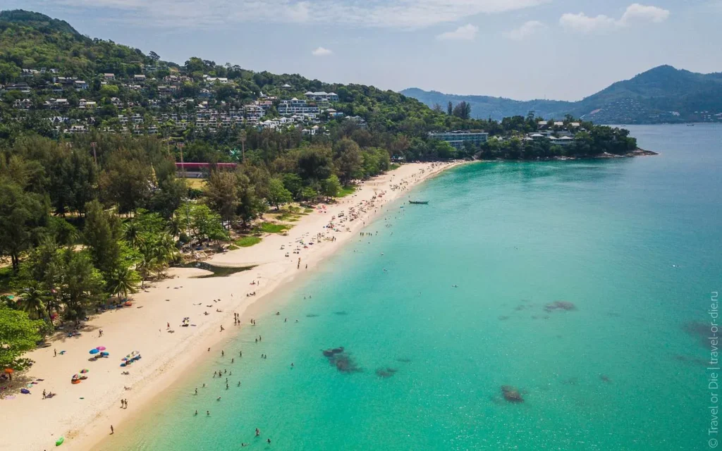 Aerial view of a tropical beach with turquoise water, white sand, and green hills in the background.