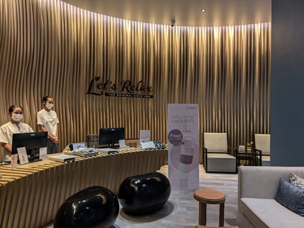 Alt text:
Reception area with two staff wearing masks, modern wooden wave wall, and black chairs.