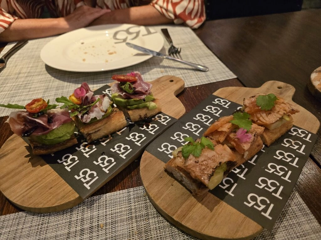 Close-up of gourmet appetizers with herbs on wooden boards at a restaurant table.