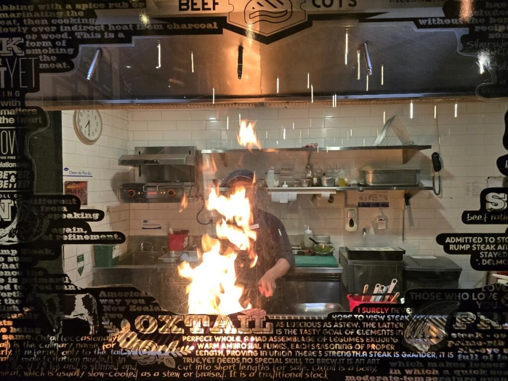 Chef cooking with large flame in open kitchen of a modern steakhouse restaurant at night