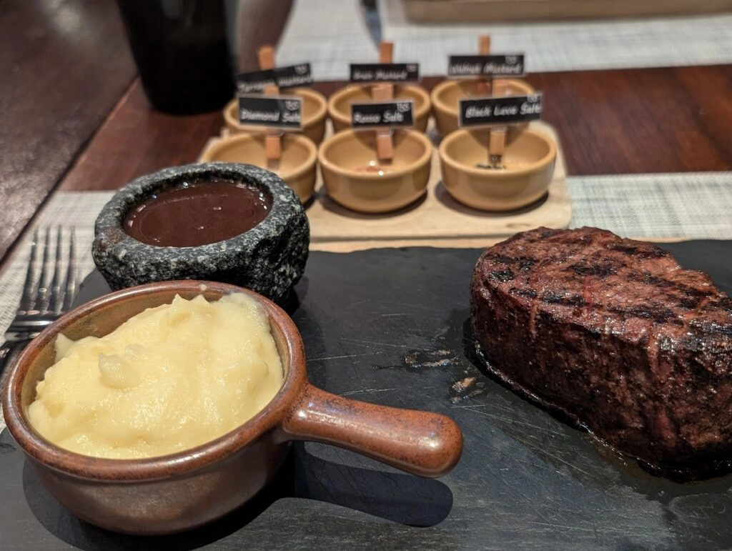 Grilled steak with mashed potatoes and six different steak sauces on a wooden table