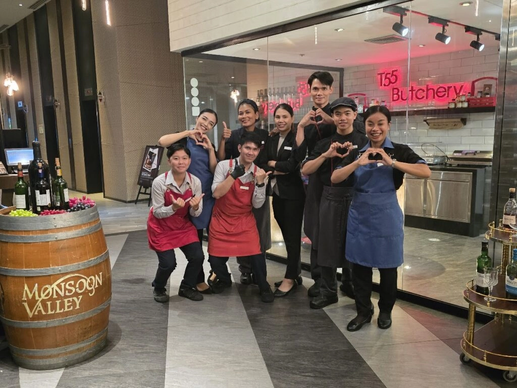 Group of restaurant staff posing and smiling inside a modern eatery near a wine barrel
