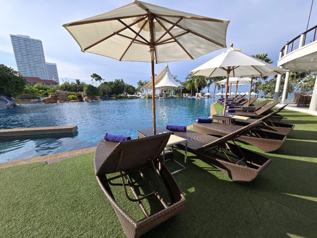 Poolside lounge chairs with umbrellas beside a large outdoor swimming pool on a sunny day