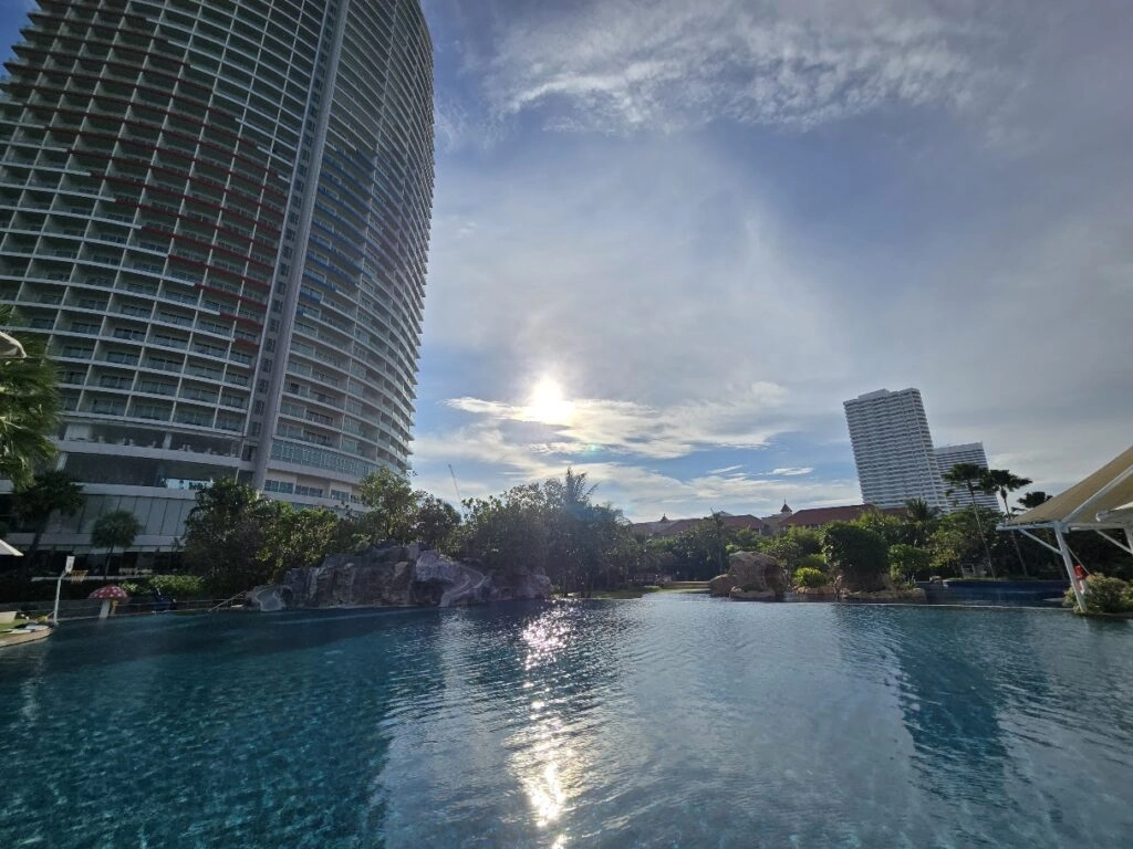 City skyline with tall buildings reflected in a calm pool under a partly cloudy sky