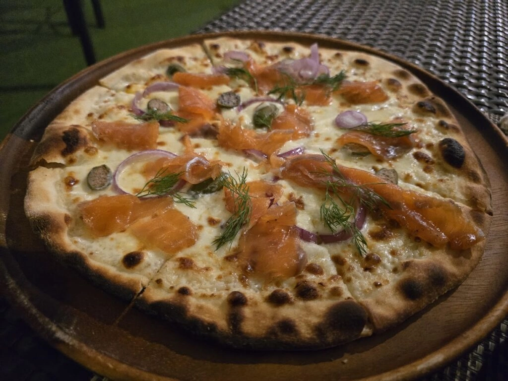 Smoked salmon pizza with red onions and dill on a wooden plate, outdoor table setting
