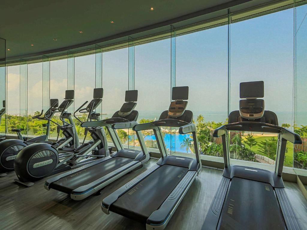 Gym with treadmills and exercise bikes overlooking a tropical outdoor pool and garden through large windows