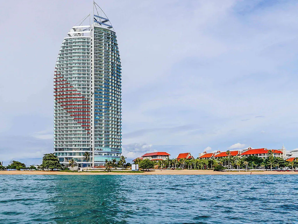 Tall modern beachfront hotel with red-roofed buildings and calm ocean water