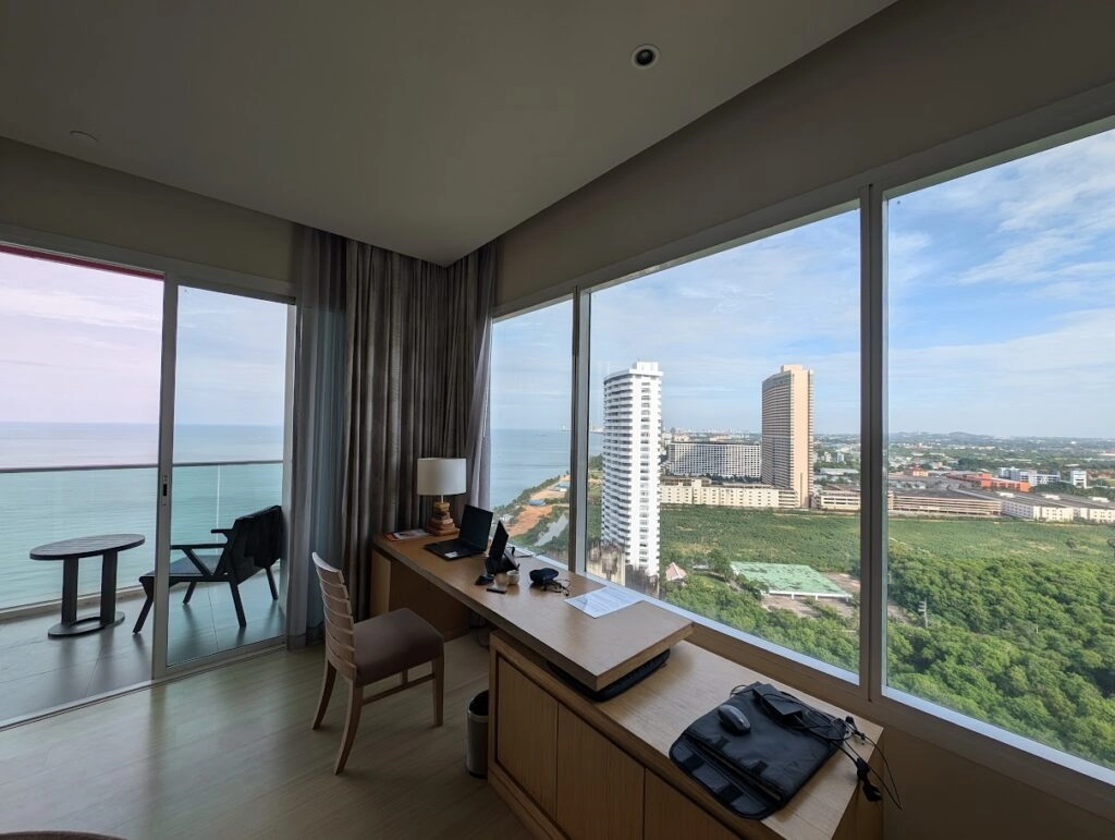 Ocean view from high-rise hotel room with desk, chair, balcony, and city skyline.