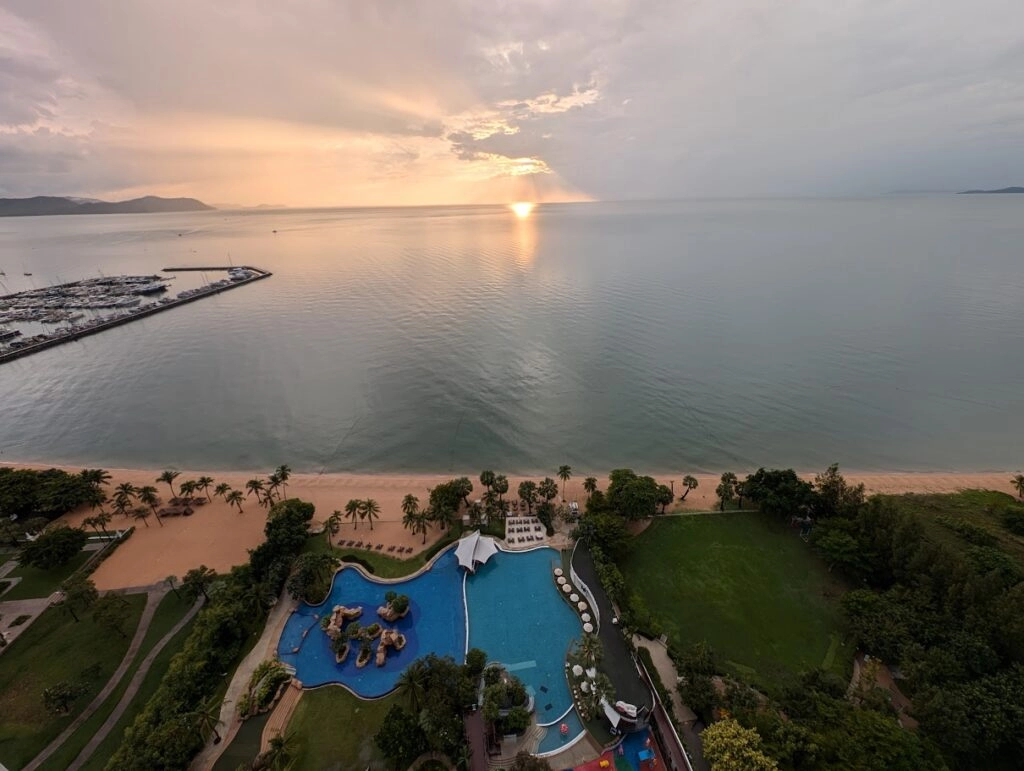 Aerial view of a beach resort pool area at sunset with calm ocean and cloudy sky.