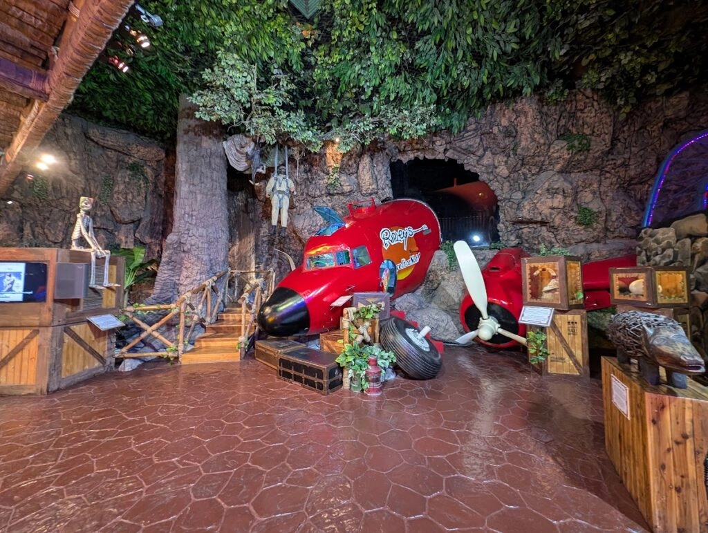 Red airplane wreck inside a cave-themed room with wooden crates and tropical decor.