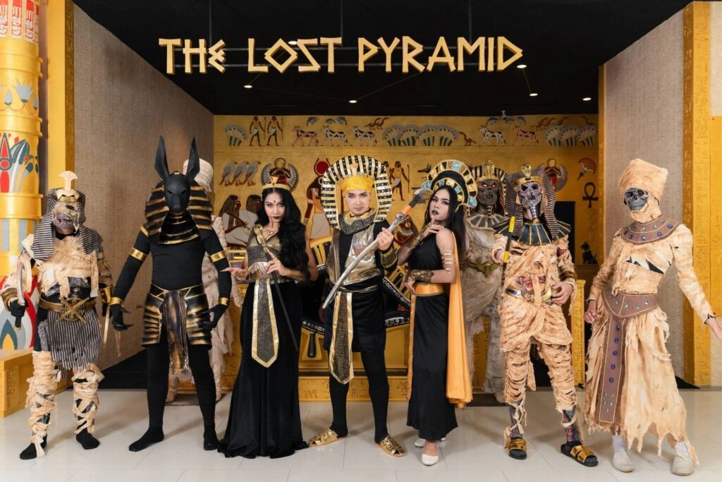 People dressed as ancient Egyptian gods and mummies posing in front of a pyramid exhibit.