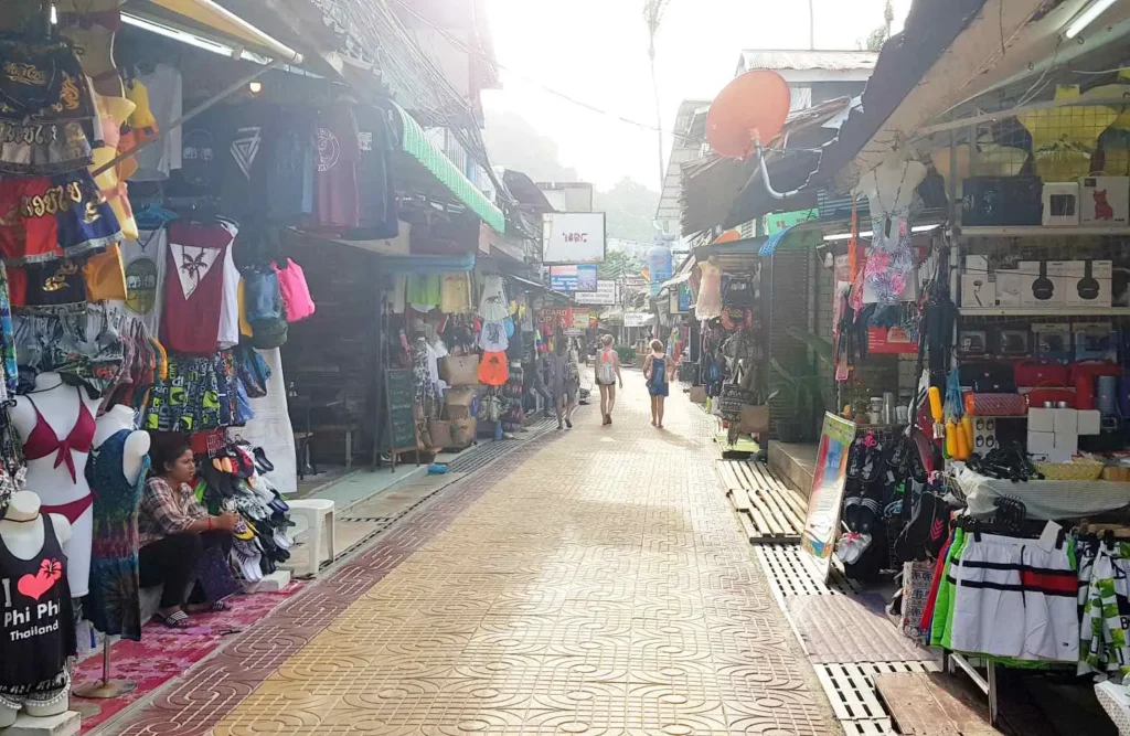 Smalle straatmarkt met kleurrijke kleding en accessoires aan beide kanten uitgestald, toeristen die rondlopen.

